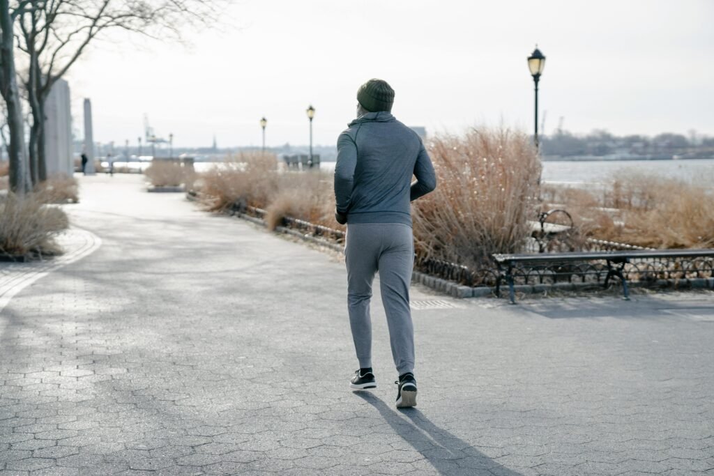 A man jogs on a scenic waterfront path surrounded by winter foliage.